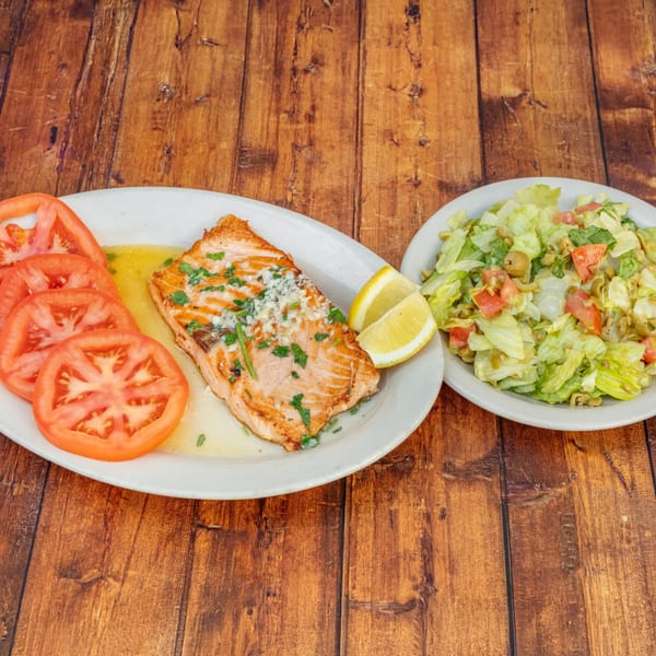 Grilled salmon with lemon, sliced tomatoes, and a side salad on a wooden table.