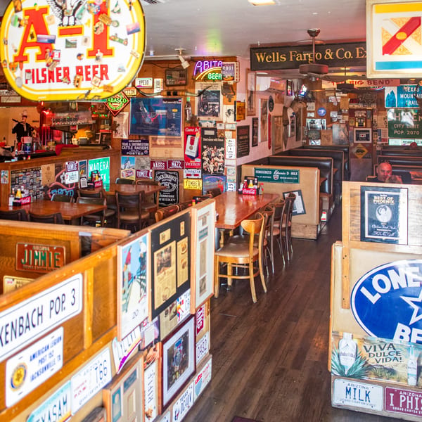 A rustic steakhouse interior with wooden tables, booths, and walls covered in vintage signs and license plates.