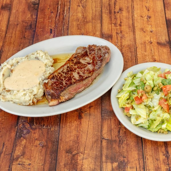 Grilled steak with mashed potatoes and gravy, alongside a fresh green salad with tomatoes and olives.
