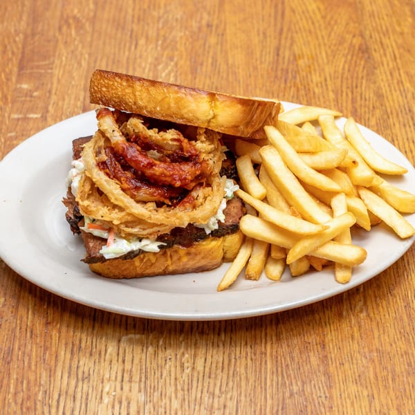 A brisket sandwich with coleslaw and onion rings, served with a side of french fries.