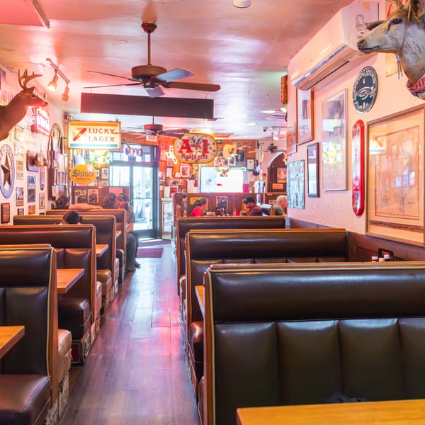 Interior of Texaz Grill steakhouse with booths, patrons, neon signs, and taxidermy deer heads.