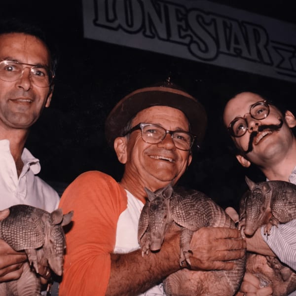 Three men smiling and holding armadillos at Texaz Grill, with a "LONESTAR" sign in the background.