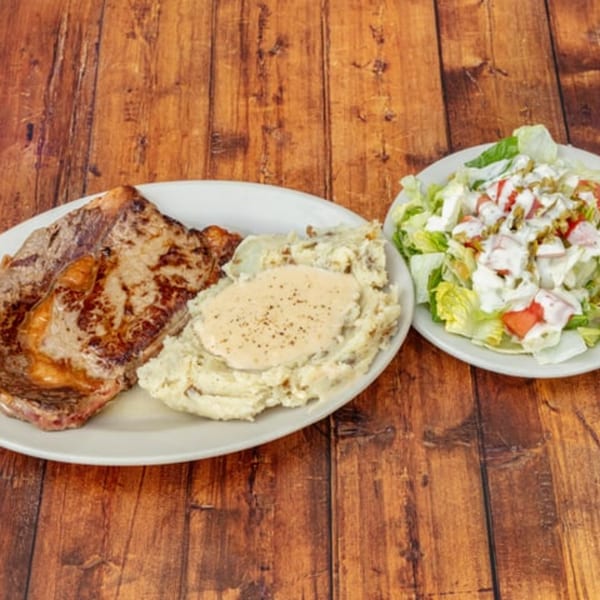 Grilled steak, mashed potatoes with gravy, and a side salad with dressing on a wooden table.