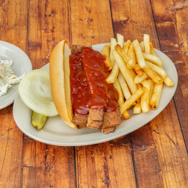 BBQ beef sandwich with fries, onion, pickle, and coleslaw on a wooden table.