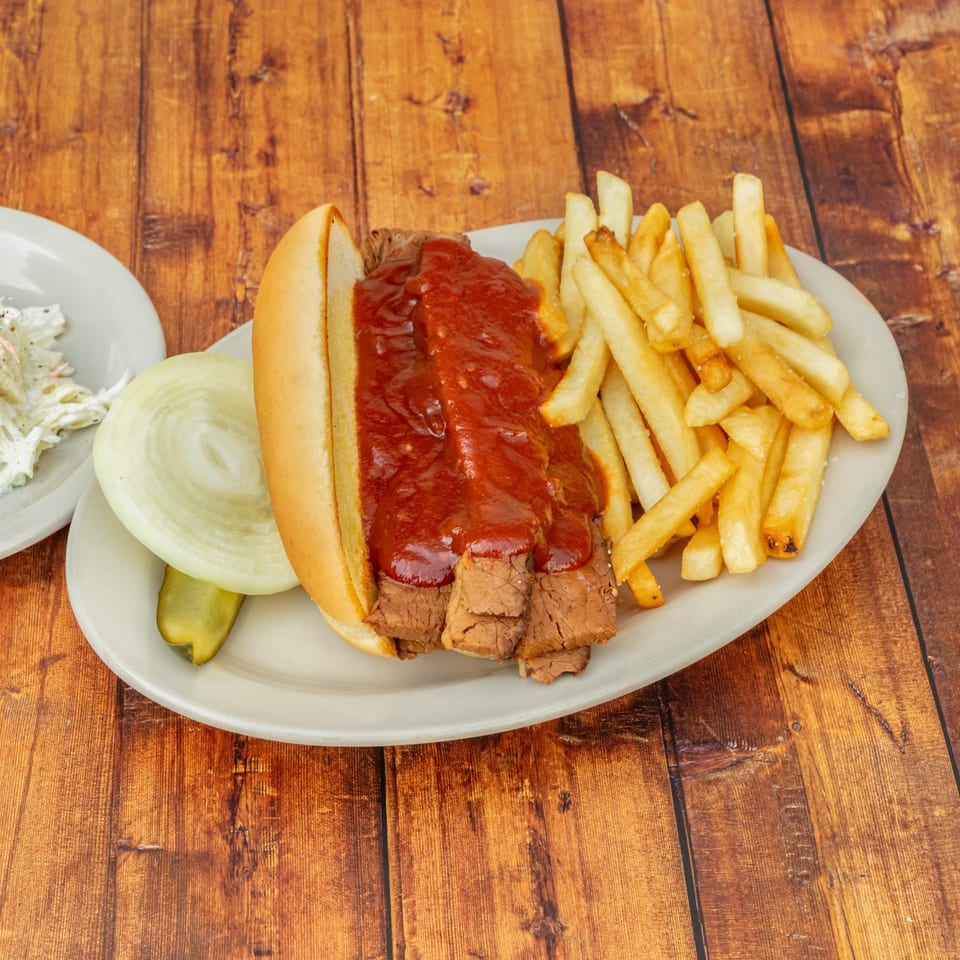 BBQ beef sandwich with fries, onion, pickle, and coleslaw on a wooden table.