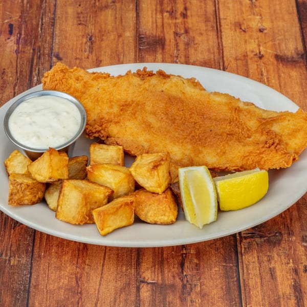 Crispy fried fish, roasted potato chunks, tartar sauce, and lemon wedges on a white plate.