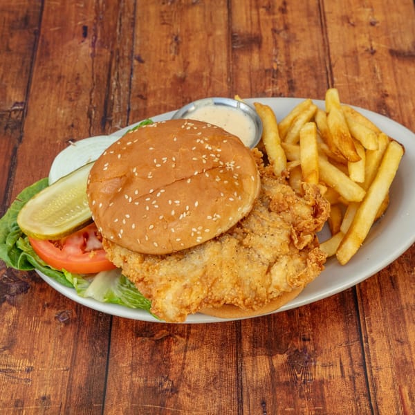 Crispy fried chicken sandwich with lettuce, tomato, onion, pickle, fries, and dipping sauce.