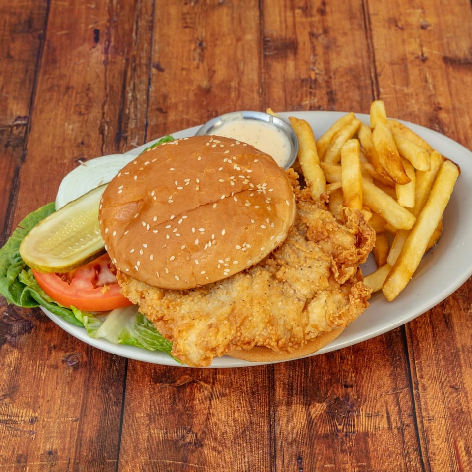 Crispy fried chicken sandwich with lettuce, tomato, onion, pickle, fries, and dipping sauce.
