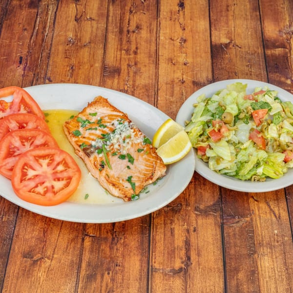 Grilled salmon with sliced tomatoes, lemon wedges, and a side salad on a wooden table.
